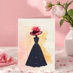 Stylish lady greeting card featuring a black maxi dress silhouette with a white constellation pattern, wearing a vibrant pink and black wide-brim feather hat, set against a soft watercolor background.
