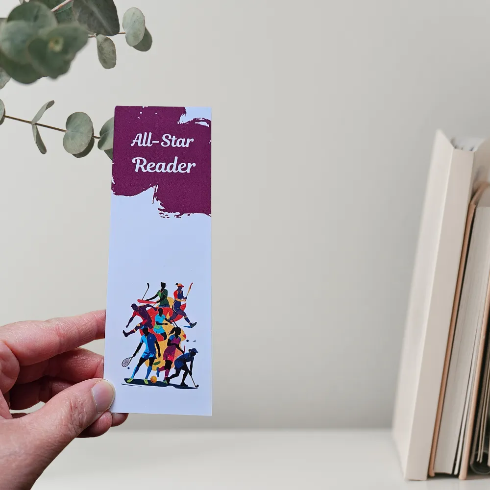 all star bookmark1 web Dynamic All-Star Reader sports bookmark featuring colorful silhouettes of diverse athletes (soccer, tennis, hockey, etc.) in action against a white background, held by a hand next to a stack of books.