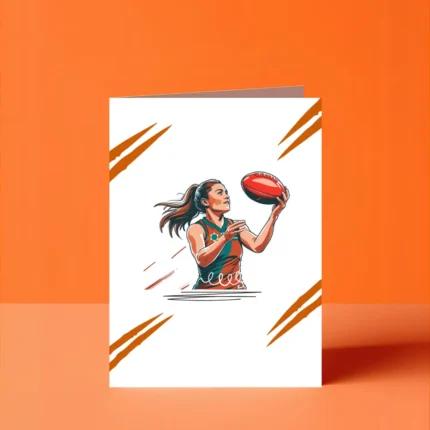 A dynamic vector illustration of a determined female Australian Rules Football (AFLW) player with a high ponytail, wearing a teal and orange jersey, holding an oval-shaped footy ball ready to kick or mark. The strong, action-oriented graphic is set against a white background with orange claw-mark accents, suitable for a collectible sports greeting card or motivational poster.