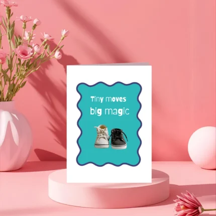 Tiny black and white baby sneakers side by side on a bright teal background with a wavy purple border, next to the text "Tiny moves big magic." New baby greeting card for first steps and baby shower gifts.