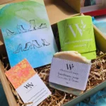 Open eco-friendly pamper gift box for women featuring handmade lavender citrus soap, a lemon myrtle bath bomb, and a stylish shoe art card resting on natural wood wool.