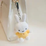 White plush bunny keychain with yellow shirt attached to a white luxury handbag.