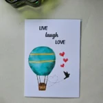 Close up of a greeting card on a textured table next to a bowl of colorful sequins.