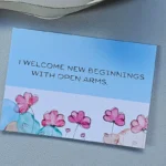 New Beginnings Greeting Card with pink watercolor flowers on a blue and white background
