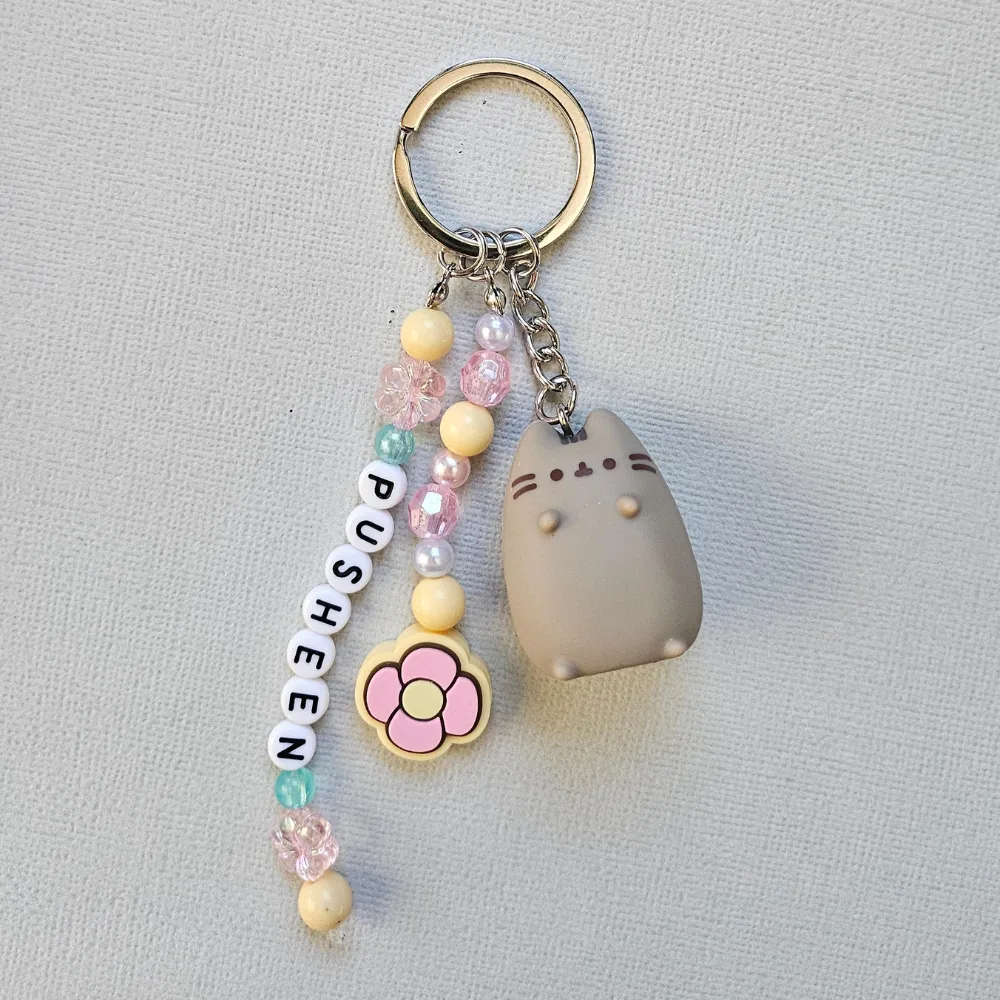 pusheen-tropical-vacation-keyring- A cute gray Pusheen Tropical Vacation Keyring with pastel pink, yellow, and blue letter beads spelling PUSHEEN, attached to a durable silver ring.