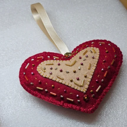 A hand-beaded crimson and cream felt heart key charm ornament with gold ribbon.