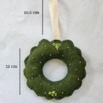 Close up of green felt wreath ornament with gold hardware and colorful beads.
