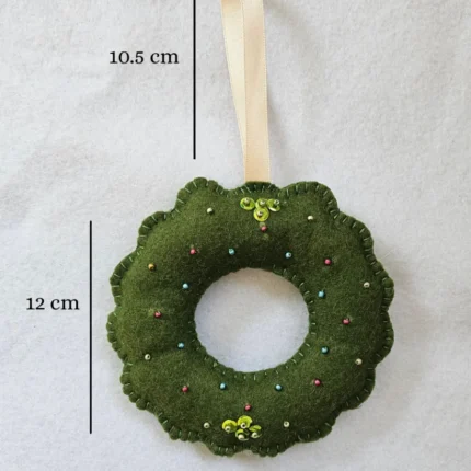 Close up of green felt wreath ornament with gold hardware and colorful beads.