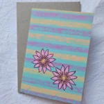 Handmade floral greeting card featuring two pink flowers on a turquoise, lavender and peach striped background.