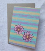 Handmade floral greeting card featuring two pink flowers on a turquoise, lavender and peach striped background.